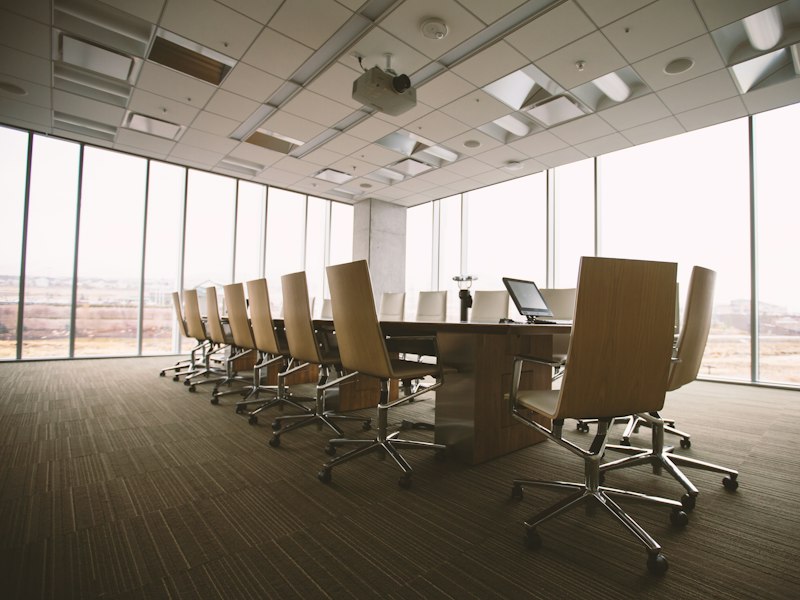 Empty boardroom with rows of chairs at a long table and floor-to-ceiling windows