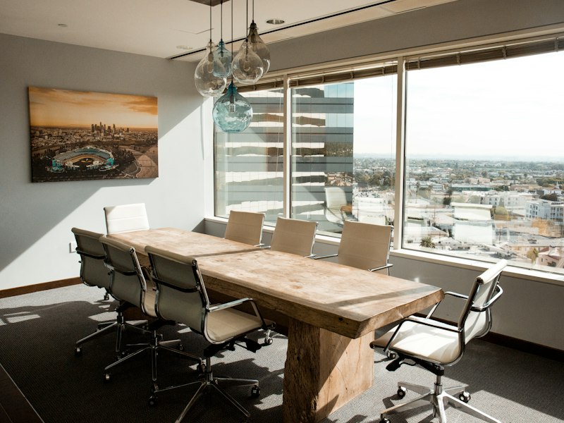 Conference room with a long wooden table and white chairs beside tall windows